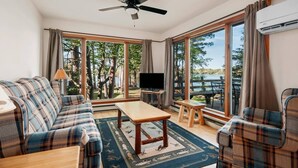 A room with a sofa, a TV, a table, and a ceiling fan. - TC Lake Stay-Pontoon & SUP Rentals-King Room! (Traverse City)