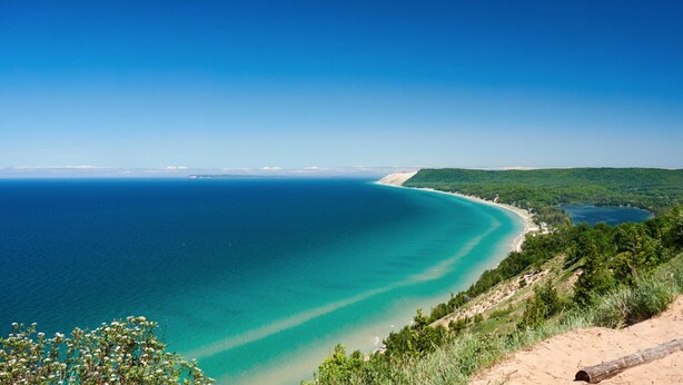 A coastal landscape with a clear view of the sea, a sandy beach, and a forested area. - Spider Lake  | Bonfires | Beach | Hot Tub l Sauna (Traverse City)