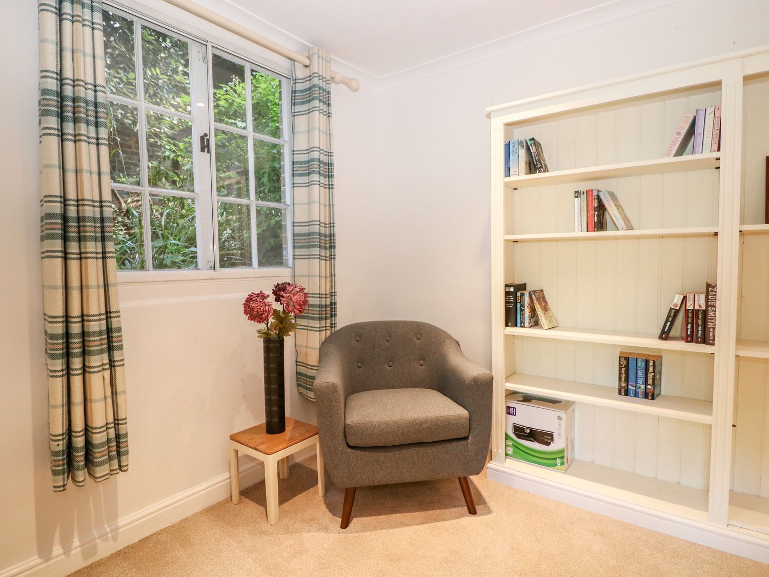 Una habitación con ventana, una silla, una mesita y una estantería.