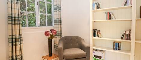 Una habitación con ventana, una silla, una mesita y una estantería.