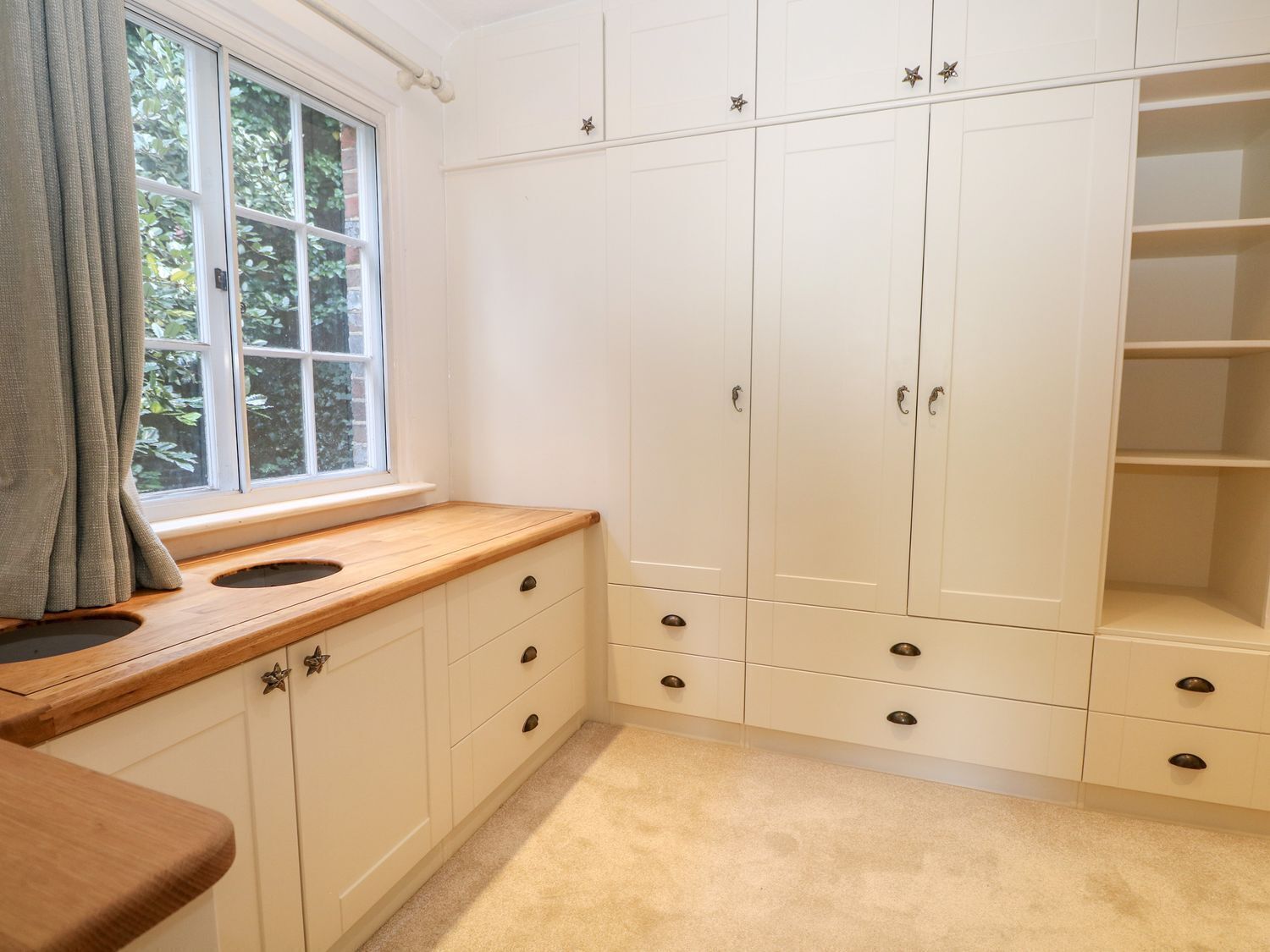 A room with a window, wooden countertop, white cabinets, and a carpeted floor.