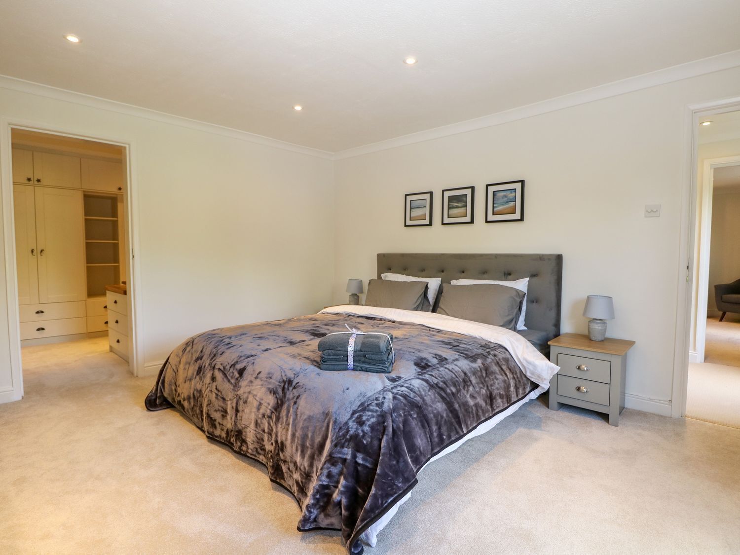 A bedroom with a large bed, a bedside table with a lamp, a wardrobe, and a door leading to another room.