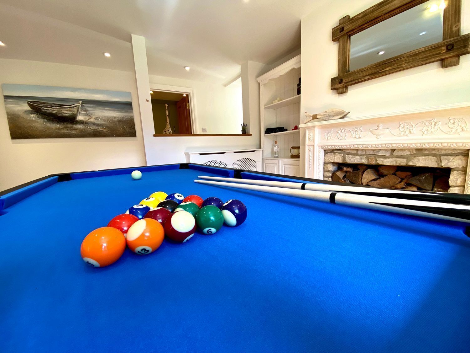 A pool table with balls, a fireplace, and a painting of a boat on the wall.