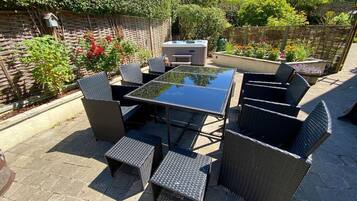 Eine Terrasse im Freien mit einem Tisch aus Glasplatten und Korbstühlen, umgeben von einem Garten mit verschiedenen Pflanzen und einem Holzzaun.