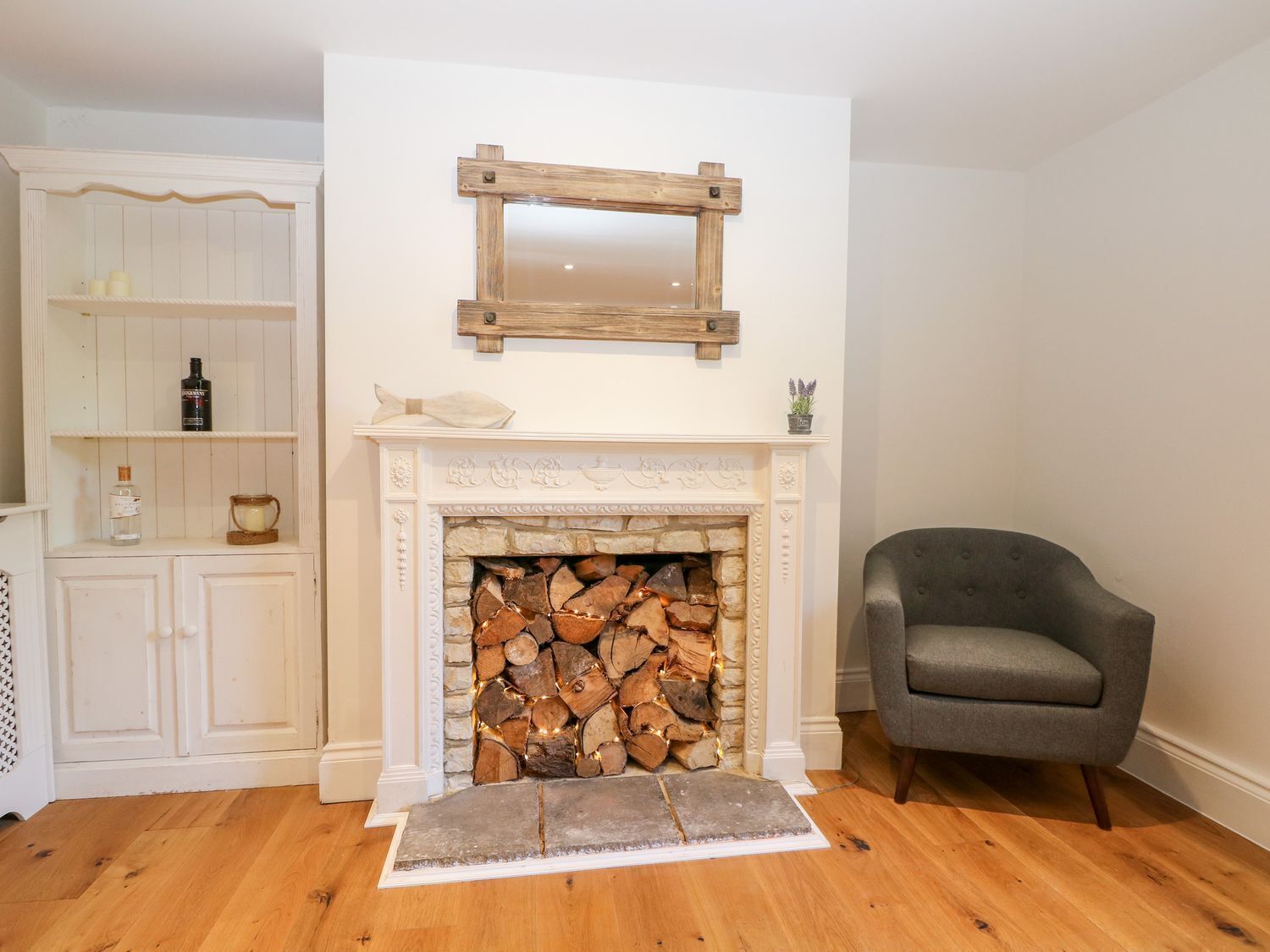 Een kamer met een open haard, een grijze fauteuil en een witte kast met planken.