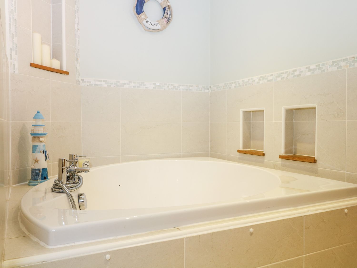 A bathroom with a bathtub, a shower, and a toilet. There are shelves with toiletries and a decorative item resembling a lighthouse.
