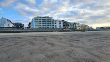 Ein Hotel an der Küste mit mehreren Etagen, einem Sandstrand davor und einem klaren Himmel.