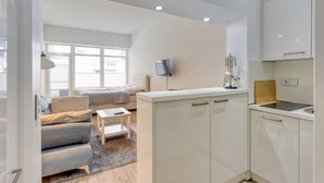 A modern, well-lit apartment with a kitchenette, a sofa, a small table, and a TV. - Alte Teestube 55 , Weststrand Wifi Kostenlos Sofortige Buchung Balkon Modernes Ein - Raum - Appartement für bis zu 2 Personen (Norderney)