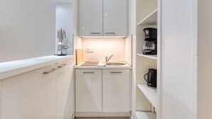 A compact kitchenette with white cabinets, a stainless steel sink, and a coffee maker. - Alte Teestube 55 , Weststrand Wifi Kostenlos Sofortige Buchung Balkon Modernes Ein - Raum - Appartement für bis zu 2 Personen (Norderney)