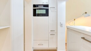 A modern kitchen with white cabinetry, a built-in oven, and a countertop with a lamp. - Alte Teestube 55 , Weststrand Wifi Kostenlos Sofortige Buchung Balkon Modernes Ein - Raum - Appartement für bis zu 2 Personen (Norderney)
