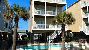 A multi-story hotel with balconies, a swimming pool, and palm trees.