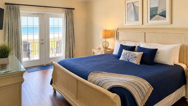 A bedroom with a bed, a nightstand, a lamp, a ceiling fan, a window with curtains, and two framed pictures on the wall.