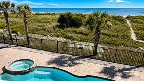 A swimming pool with a view of the ocean, surrounded by a fenced patio area with palm trees.