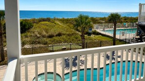 A pool area with a view of the ocean, a hot tub, and a deck with lounge chairs.