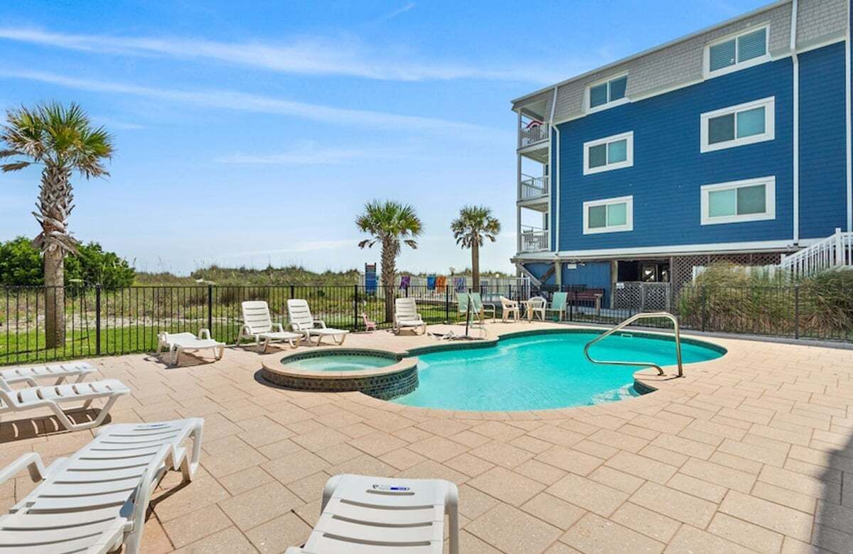 A pool area with lounge chairs, a hot tub, and a building with balconies.