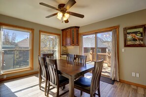 A dining area with a wooden table and chairs, a ceiling fan, and large windows with curtains.