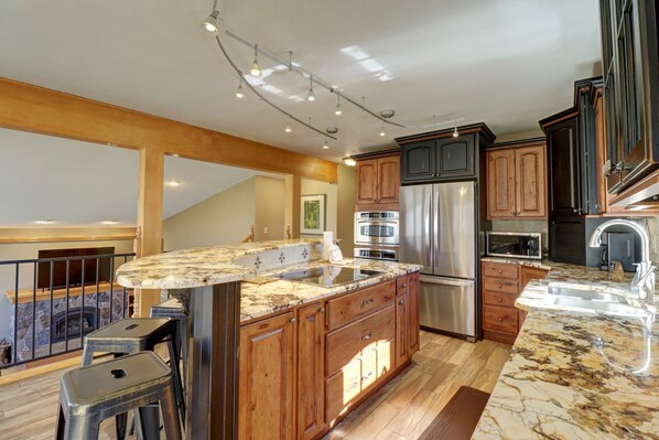 A spacious kitchen with a large island, wooden cabinets, stainless steel appliances, and a stone countertop.