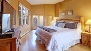 Ein geräumiges Schlafzimmer mit einem großen Bett, einem hölzernen Kopfstück und einem Fernseher auf einer Holzkommode.