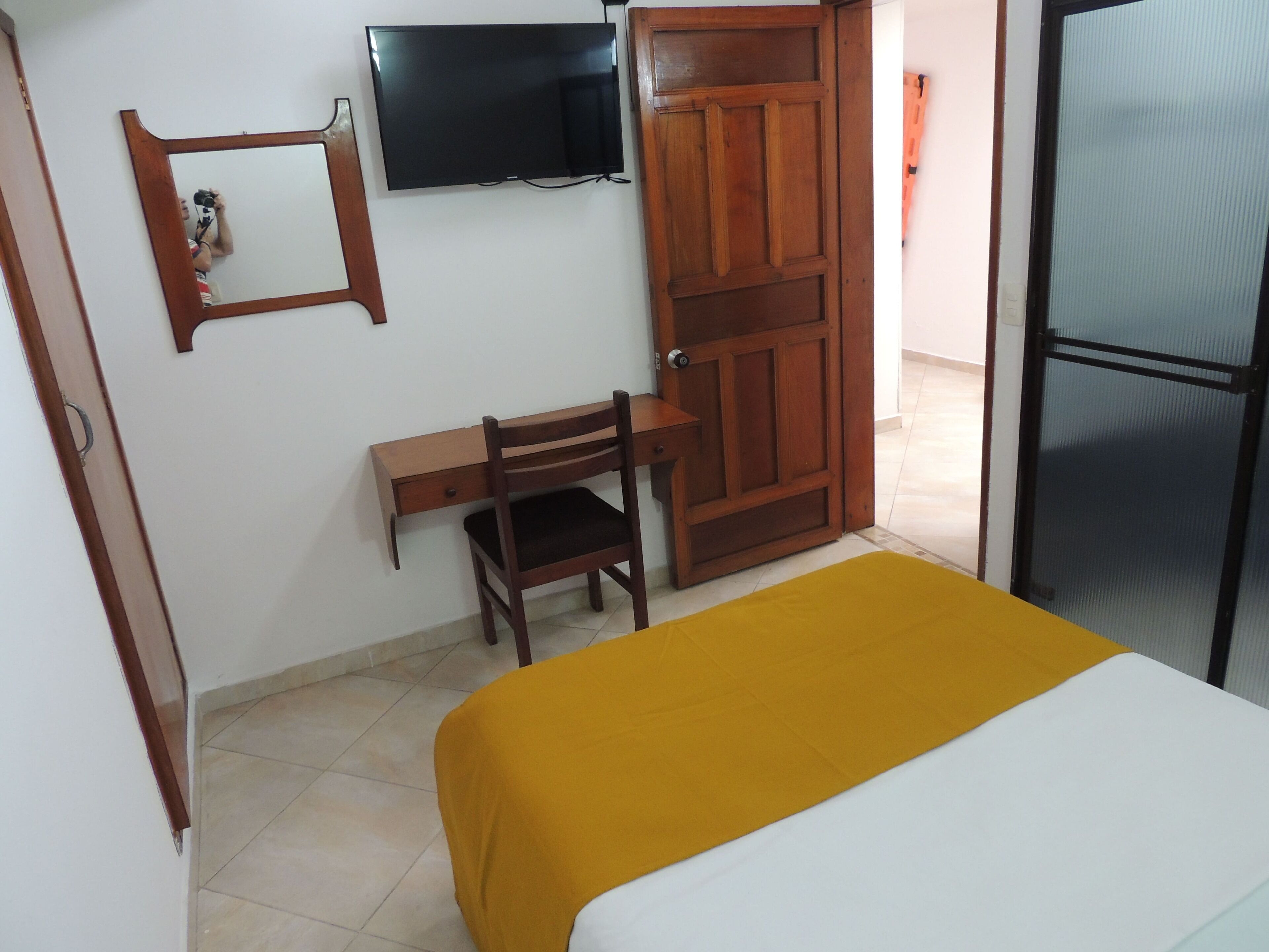Una habitación con una cama, un escritorio, una silla, un televisor y una puerta.
