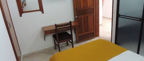 Una habitación con una cama, un escritorio, una silla, un televisor y una puerta.