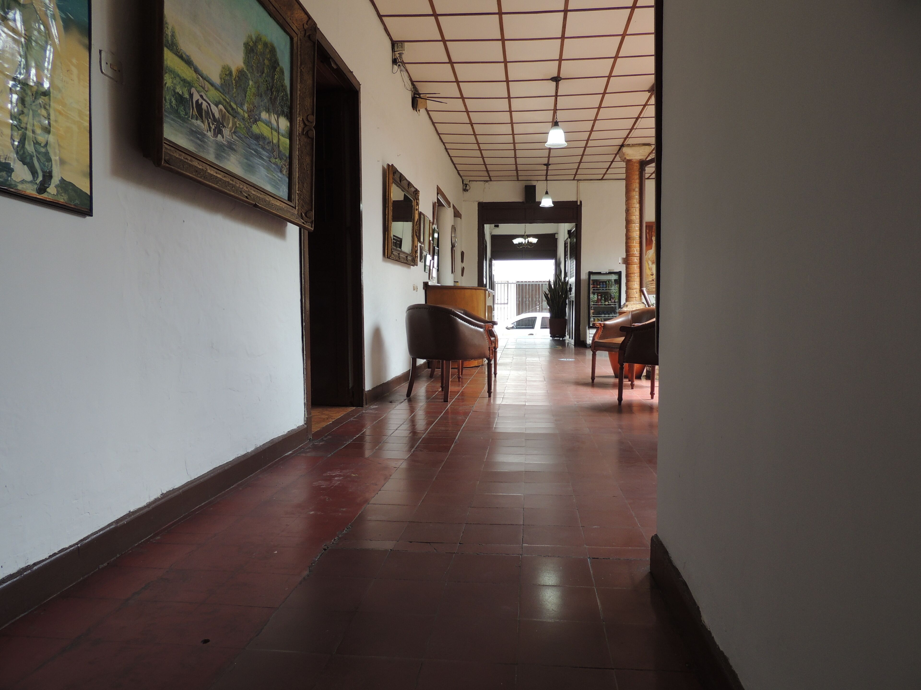 A hallway with a tiled floor, a painting on the wall, and a door leading to another room.