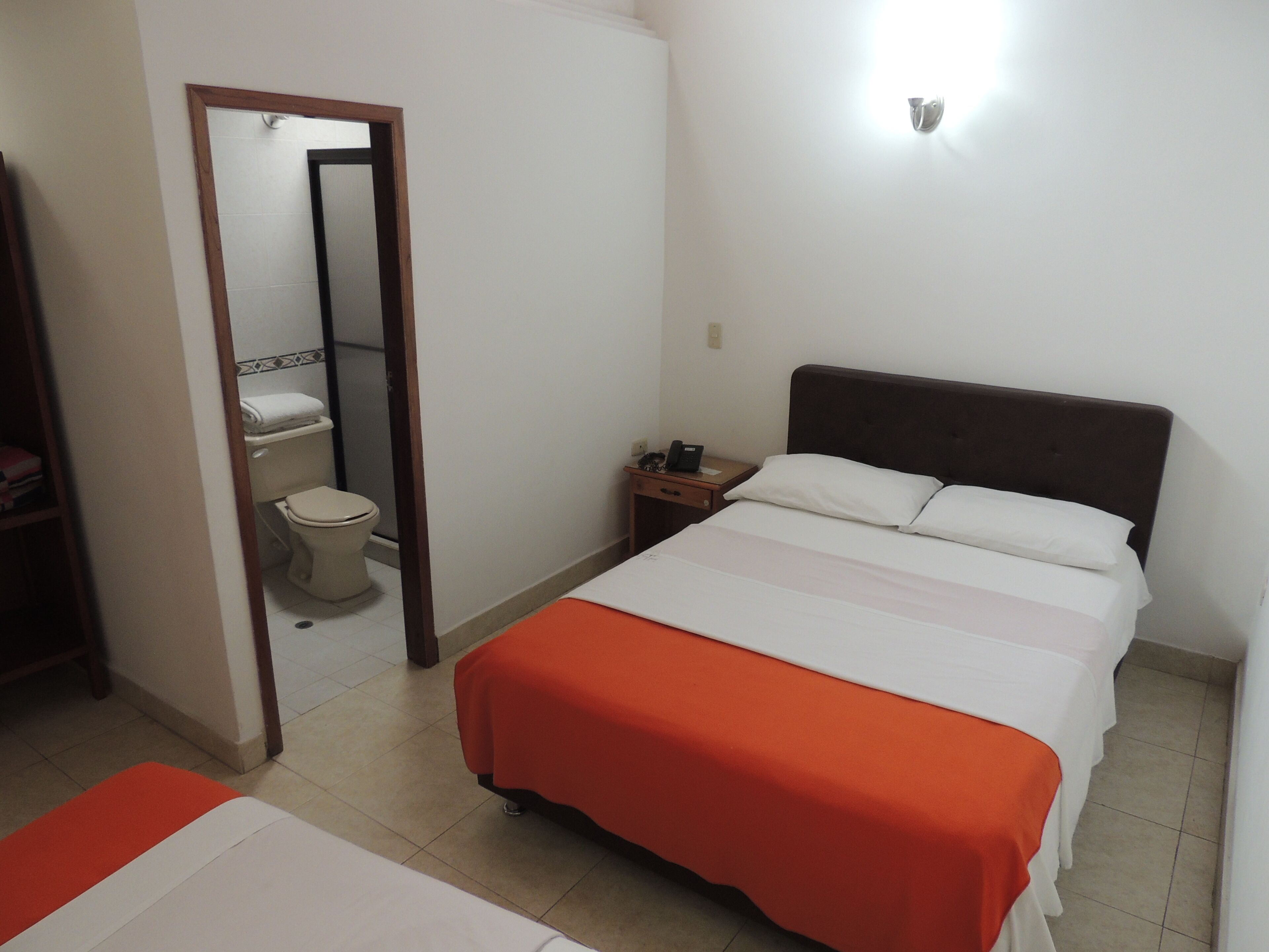 Una habitación de hotel con cama, mesita de noche, espejo y un inodoro.