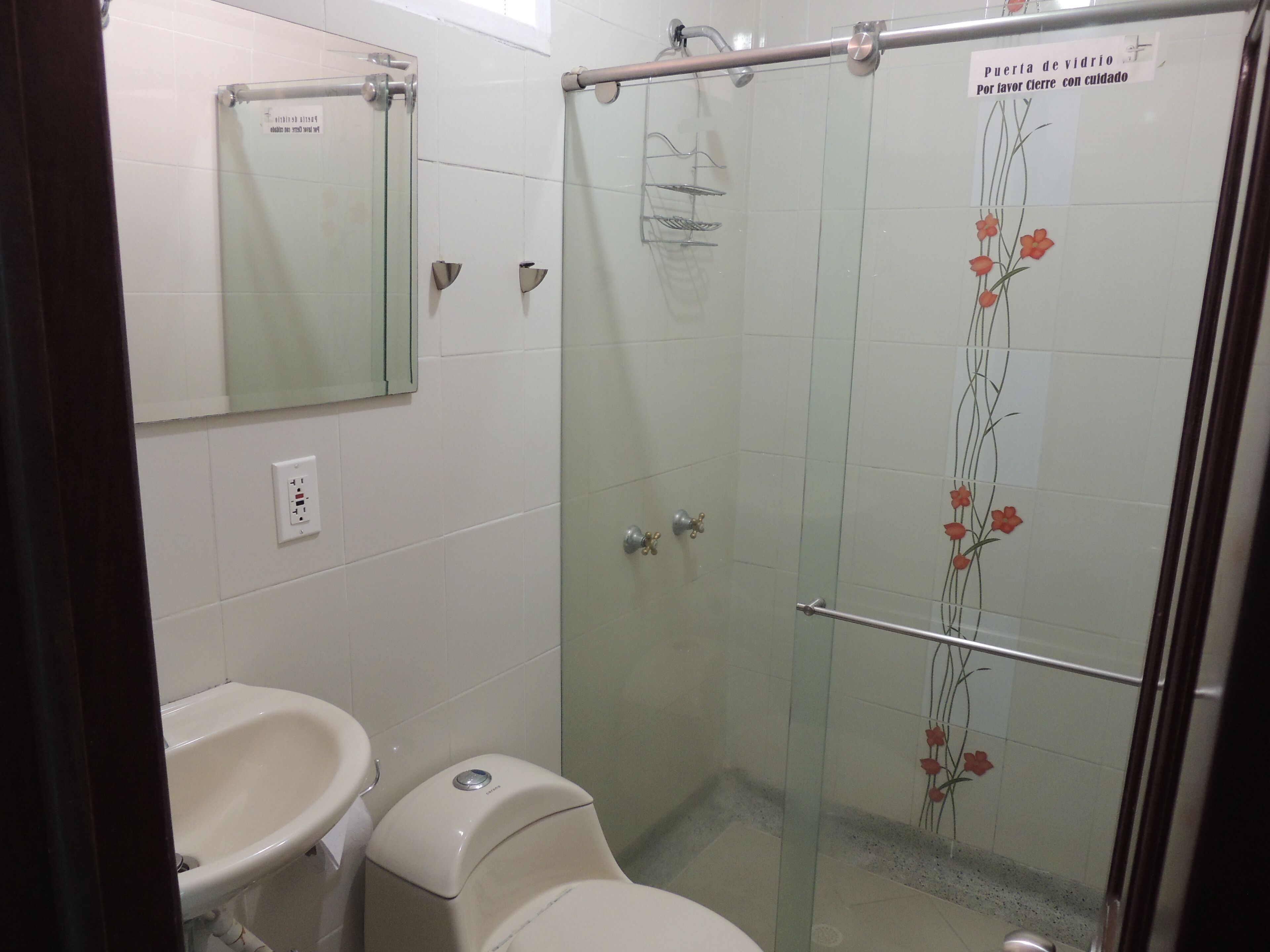 A bathroom with a glass shower enclosure, a toilet, and a sink.
