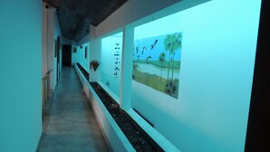 A corridor with a tiled floor, a wooden ceiling, and a wall with a painting of birds and palm trees. - HOTEL REAL (Ocaña)