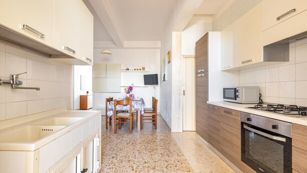 A modern kitchen with white cabinets, a granite countertop, a built-in oven, and a dining area with a table and chairs. - 2529 Aura Apartments - Trilo Asia PP SX by Barbarhouse (Porto Cesareo)