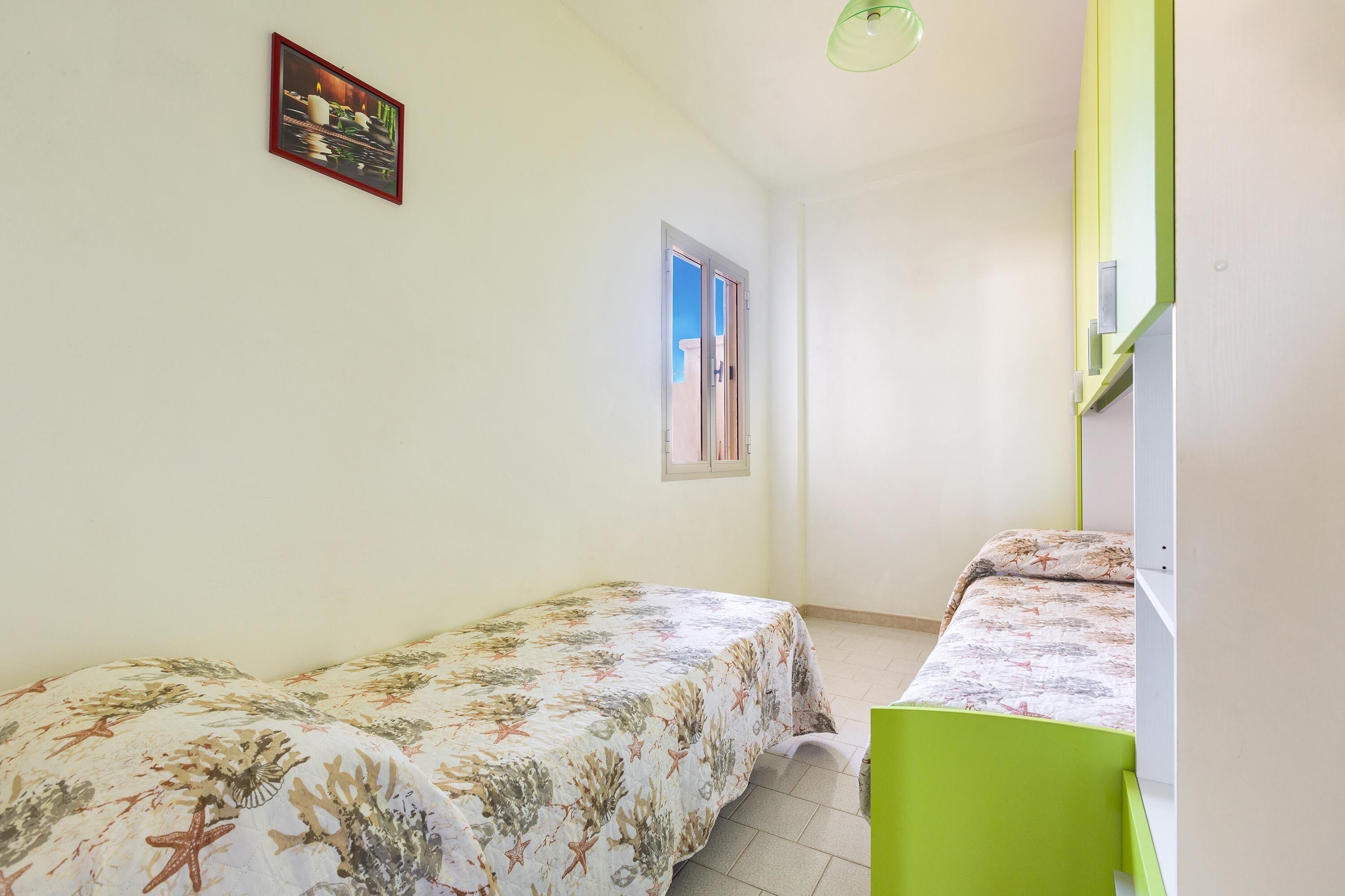 Une petite pièce propre, avec deux lits, une fenêtre et une chaise verte.
