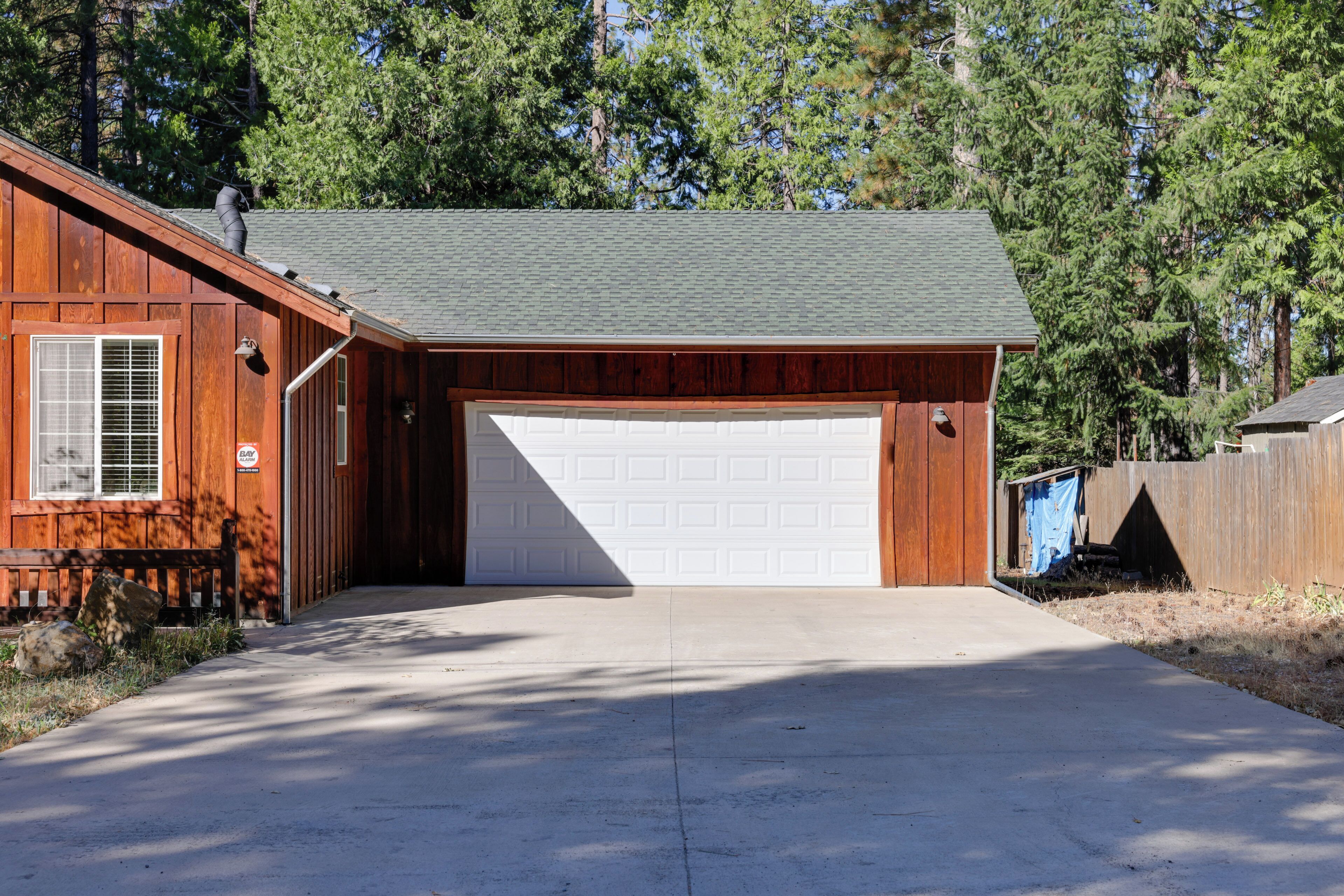 Een gelijkvloers houten huis met een garage, een voortuin en een oprit die naar de garage leidt.