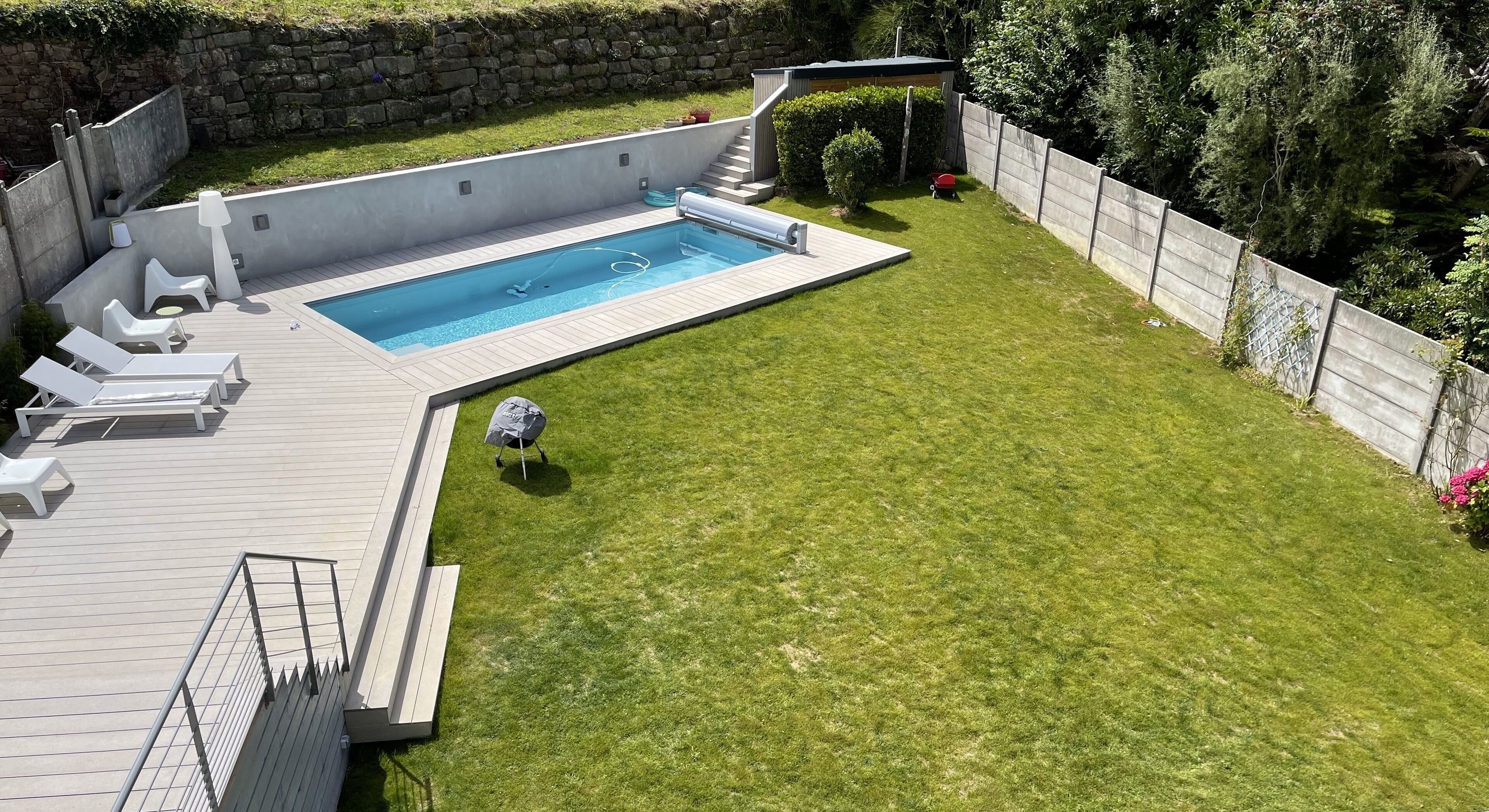 A backyard with a swimming pool, a wooden deck, and a grassy lawn.