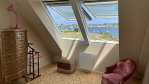 A room with a sloped ceiling, a wooden dresser, a pink chair, and a view of a body of water through skylights. - Villa Avec vue Mer, Piscine Chauffée (Landéda)