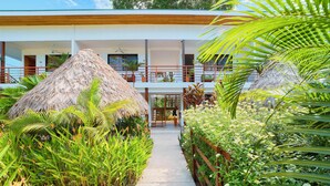A modern building with a central courtyard, surrounded by lush greenery and thatched-roof structures. - Olinca Boutique Hotel (Cahuita)