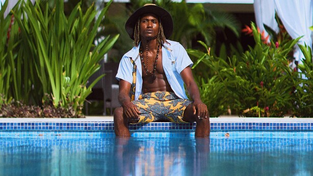 A person sitting by a pool with a tiled edge, surrounded by greenery and a building with a balcony in the background. - Olinca Boutique Hotel (Cahuita)