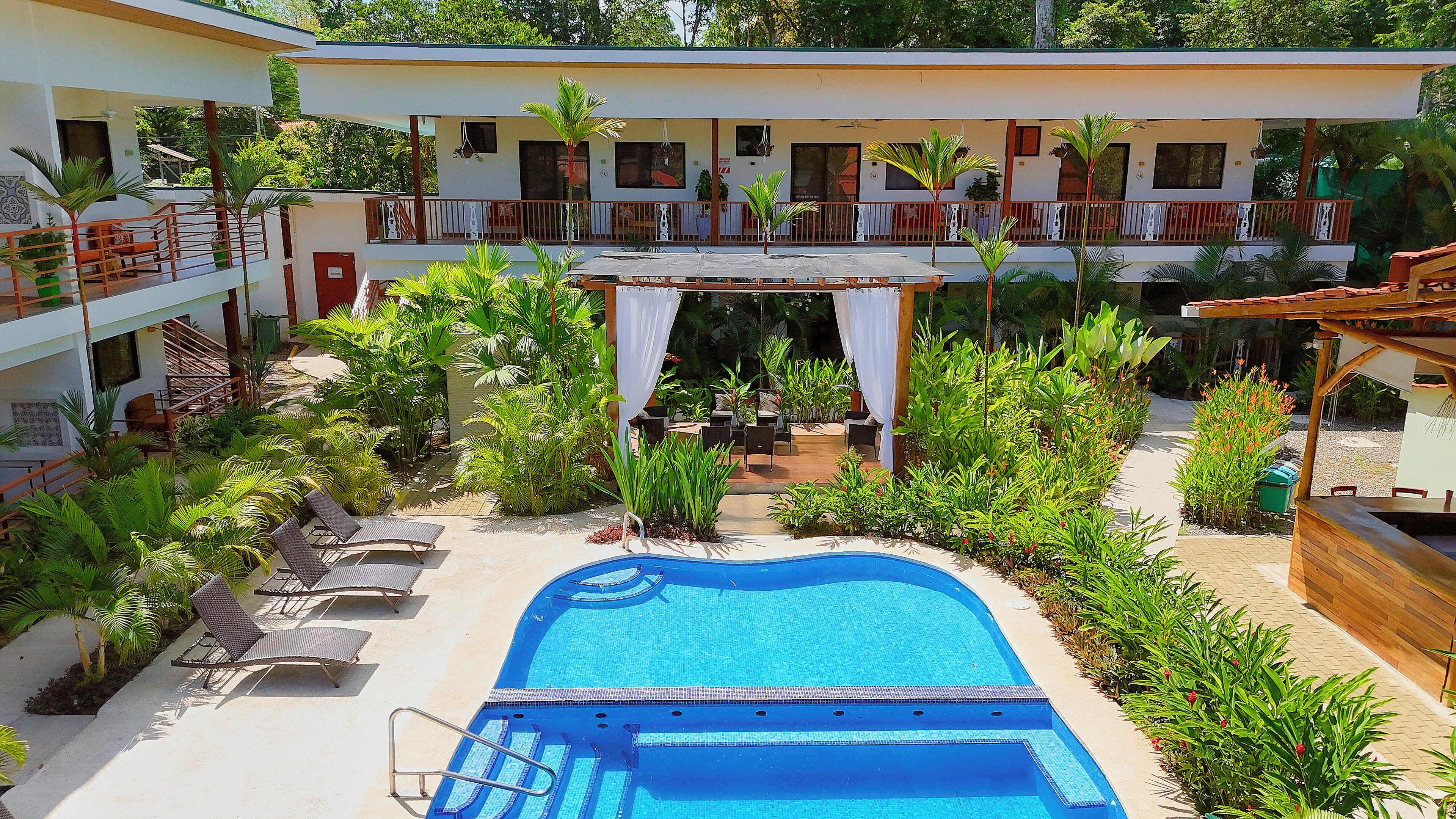 A hotel with a swimming pool, outdoor seating, and lush greenery.