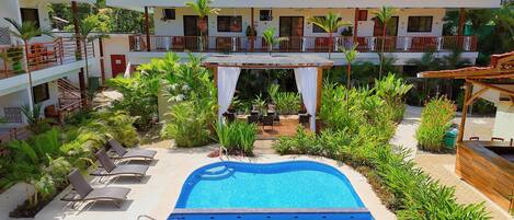 A hotel with a swimming pool, outdoor seating, and lush greenery.