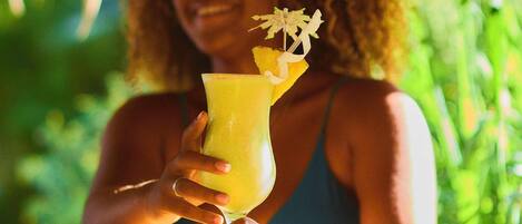 A person holding a drink with a decorative garnish, seated at a wooden table outdoors.
