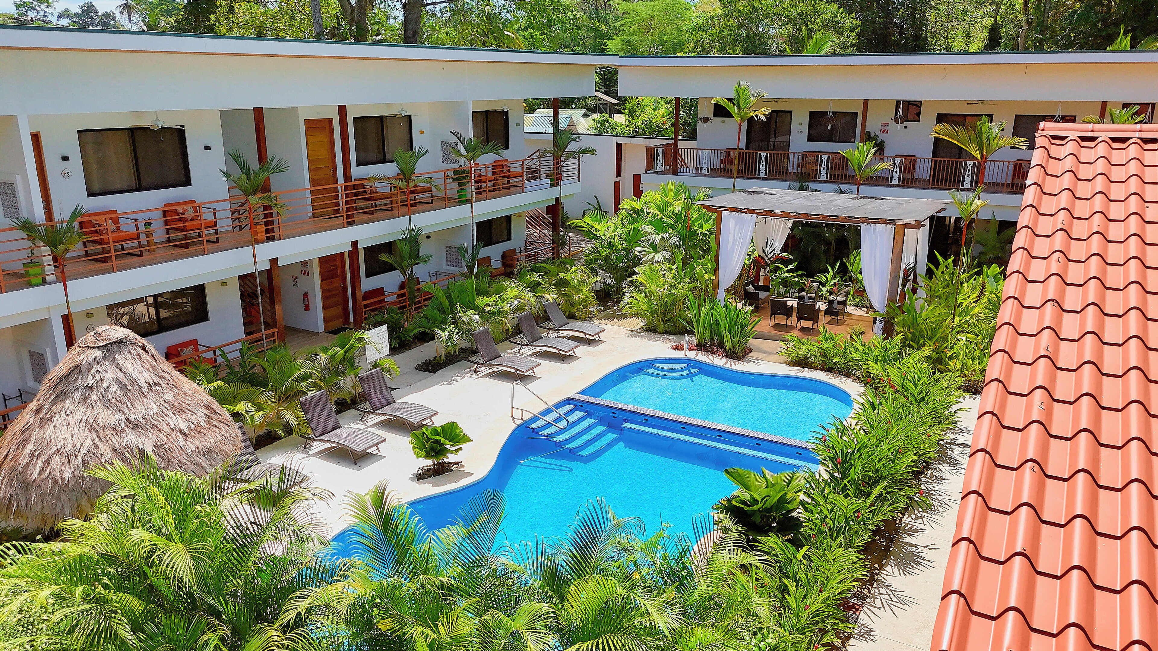 A hotel with a swimming pool surrounded by lush greenery, multiple balconies, and outdoor seating areas.