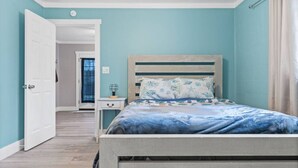 A bedroom with a bed, bedside table, and a door leading to another room. - Cozy Cottage Walking Distance to the Beach With Coffee Bar (Oak Island)