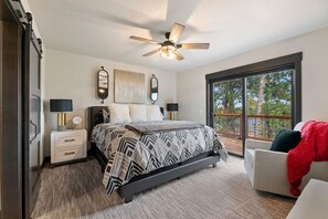 A bedroom with a bed, bedside tables, a ceiling fan, a large window with a view of trees, and a balcony. - Make Time Lodge- Clubhouse Access, Outdoor fireplace/Seating, Hot Tub, & Garage  (Lead)
