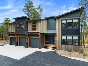 A modern two-story house with a garage, wooden exterior, and large windows. - Make Time Lodge- Clubhouse Access, Outdoor fireplace/Seating, Hot Tub, & Garage  (Lead)