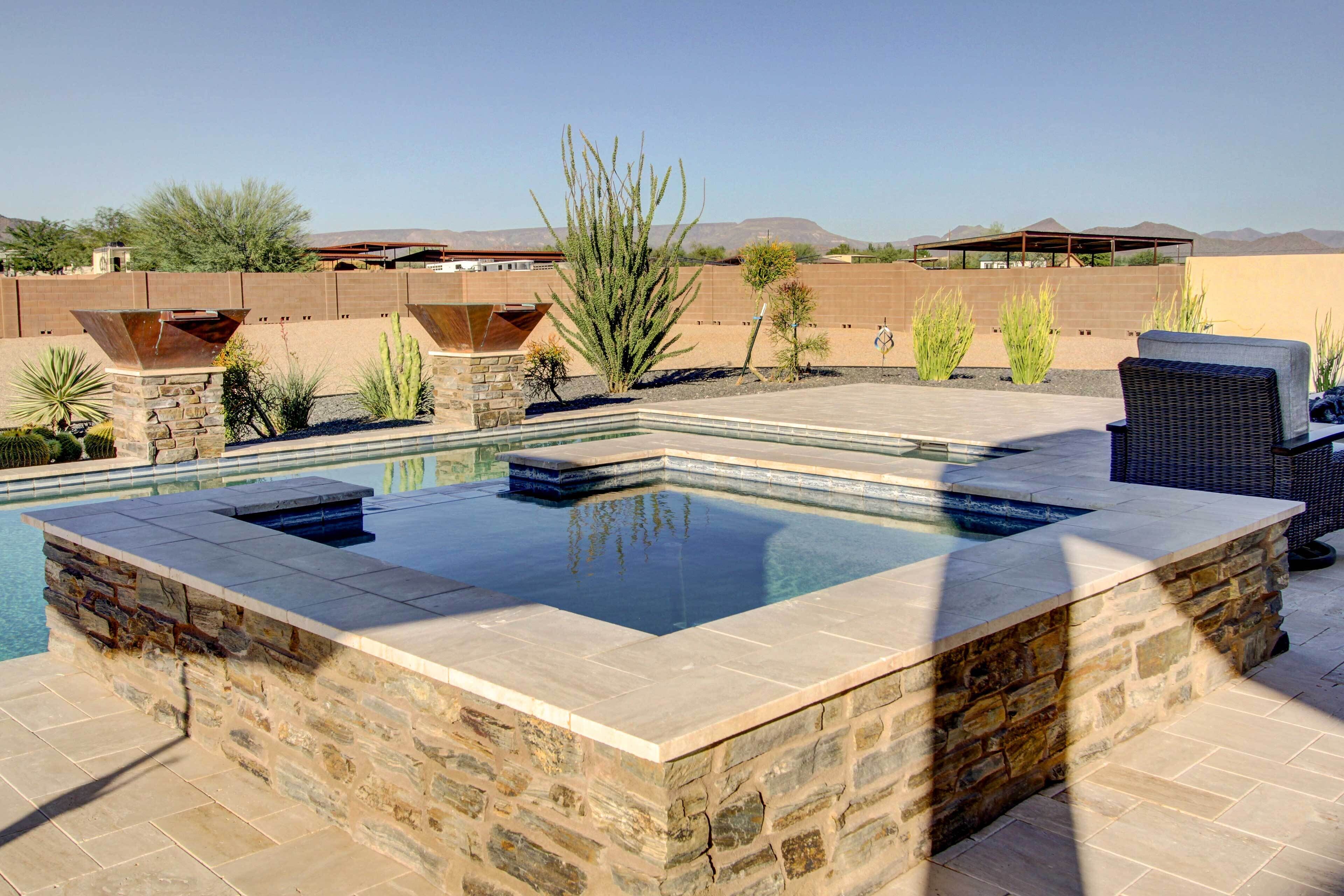 A swimming pool with a stone surround and a seating area with wicker furniture.