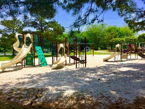 Children can play safely on the playground's slides, climbing frames, and sandpit surrounded by trees.