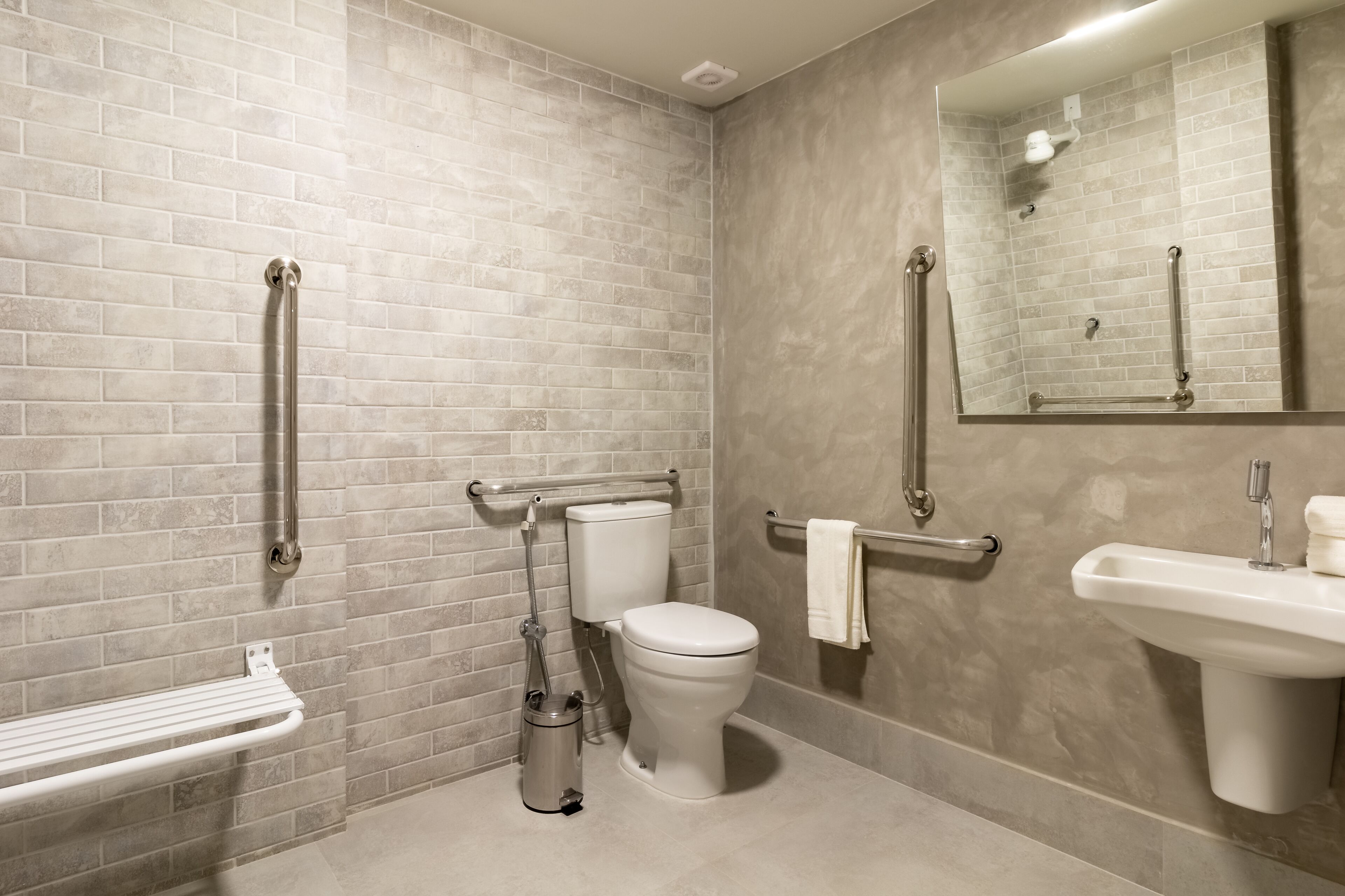 Une salle de bain moderne équipée de toilettes, d’un bidet et d’un lavabo, ainsi que de barres d’appui et d’une main courante.