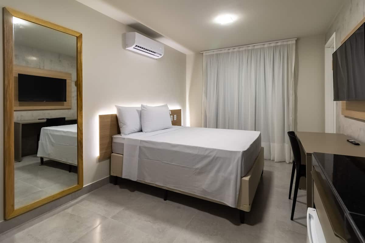 A modern hotel room with a large bed, a desk, a mirror, and an air conditioning unit.