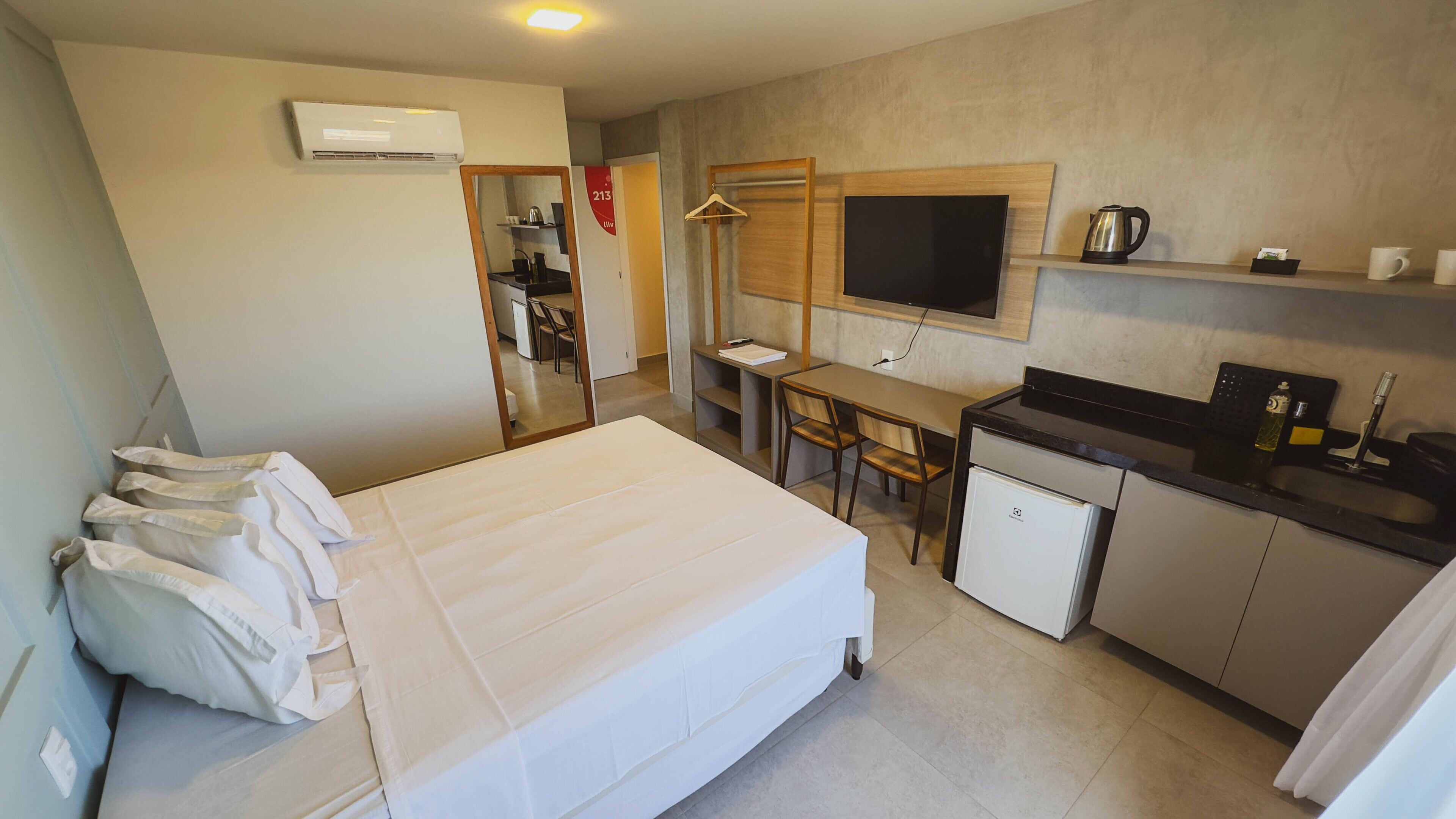 Ett kompakt hotellrum med en säng, ett litet skrivbord, en tv, ett litet pentry och en garderob.