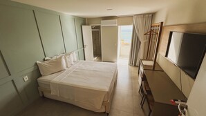 Habitación de hotel con cama, televisión, escritorio y baño visible a través de una puerta abierta.