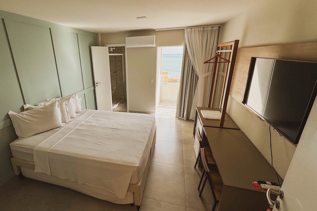A hotel room with a bed, a TV, a desk, and a bathroom visible through an open door.