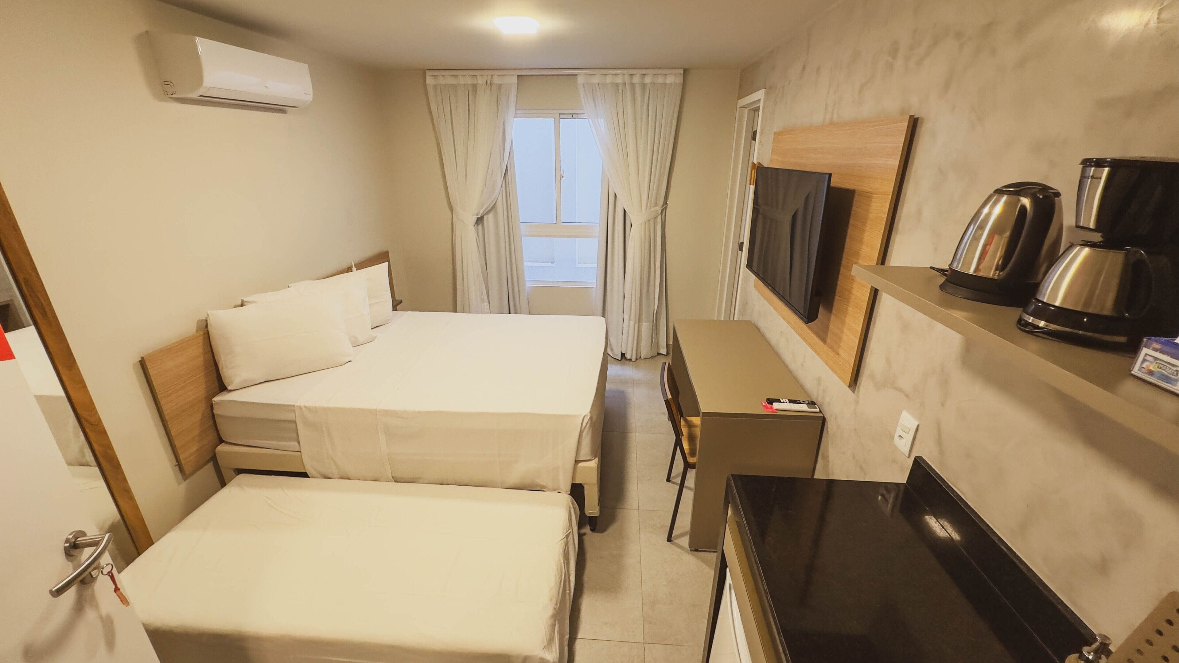 A hotel room with two beds, a TV, a coffee maker, and a desk.